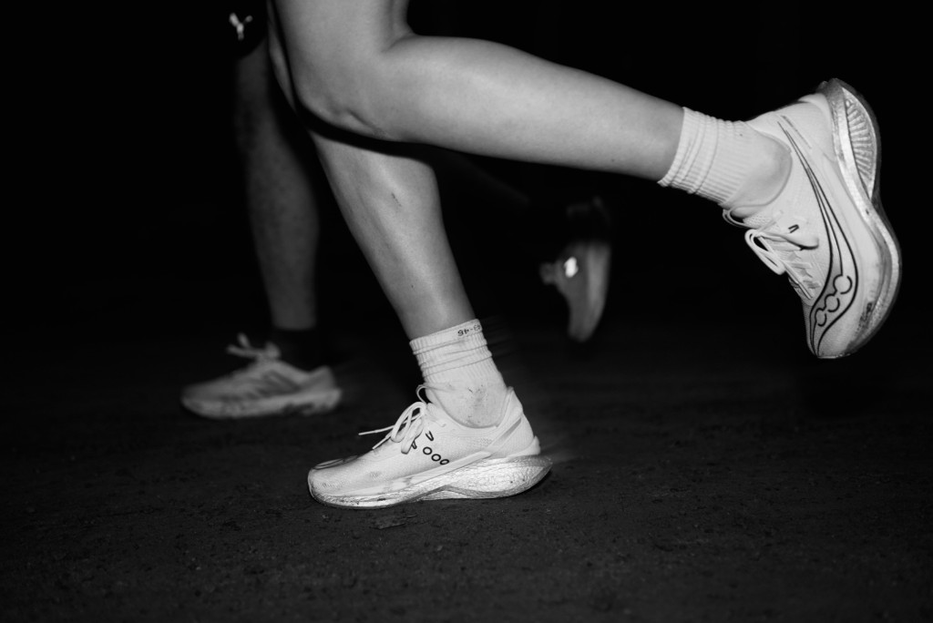 Runners’ feet in white shoes mid-stride on a dark road at night